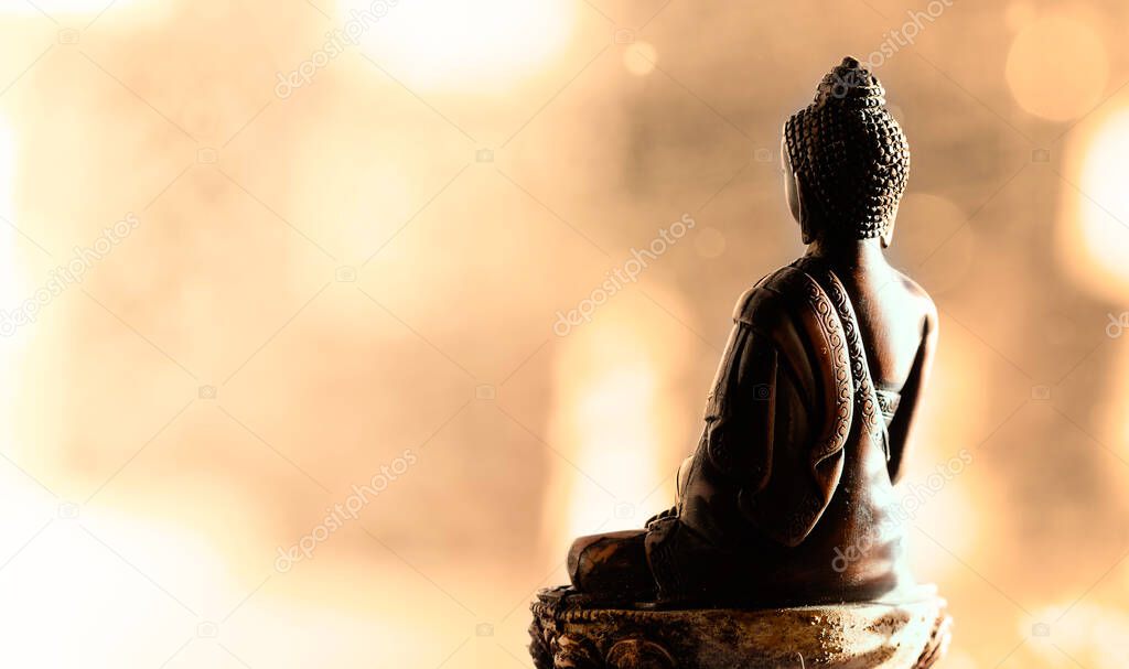 Back side of meditating Buddha statue. Bokeh background. Warm colors. Peace of mind concept