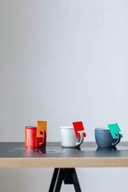 Gri arkaplanda mavi bir masada farklı renkte çay fincanları..