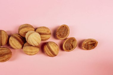 Lezzetli cevizli sandviç kurabiyeleri. Yoğunlaştırılmış süt ve kahverengi kil tabakta fıstık. Pembe arka planda, yukarıdan görüş, yakın plan. Yüksek kalite fotoğraf