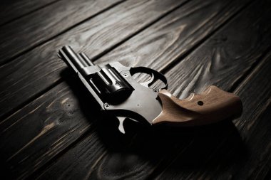 Siyah revolver tabancası koyu ahşap arka planda.