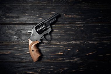 Siyah revolver tabancası koyu ahşap arka planda.