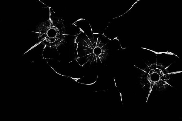 отверстия от пуль в стекле крупным планом на черном фоне