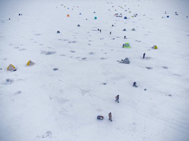Donmuş gölde kış balıkçılığı. Gölün buzuna monte edilmiş renkli balıkçı çadırları. Hava görünümü.