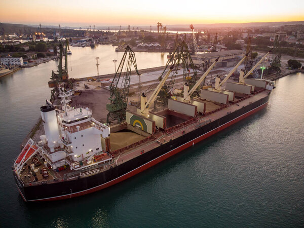 Aerial top view of big cargo ship bulk carrier is loaded with grain of wheat in port at sunset