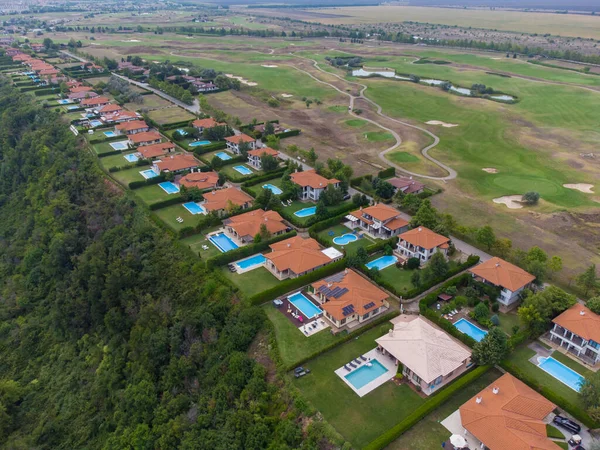 Modern cottage village with luxury houses, swimming pools and golf courses aerial top view.