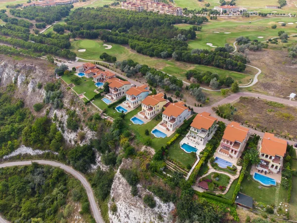 Modern cottage village with luxury houses, swimming pools and golf courses aerial top view.