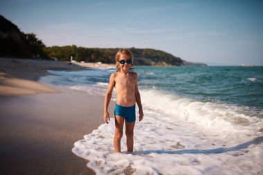 portrait of a long haired 8 year old boy in blue swimming goggles against the backdrop of the sea on a on a summer evening