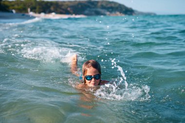 8 years old boy swims in the sea in blue swimming goggles in the evening