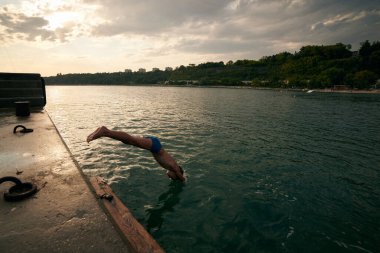 8 years old boy dives into the sea from a pier. Hot summer day.