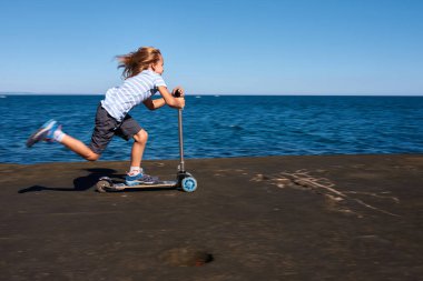 Güneşli bir günde iskelede scooter süren bir çocuk.