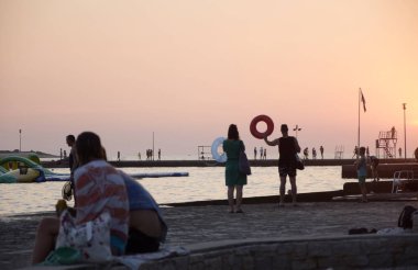 İnsanlar iskelede, Adriyatik Denizi 'nde, Porec' te, Istria 'da, Hırvatistan' da yürüyor. Gün batımı ve deniz.