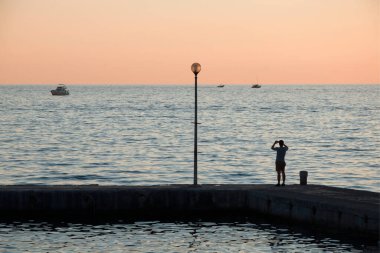 Gün batımında rıhtımda. Adriyatik denizi, Porec, Hırvatistan. Rıhtımdaki bir insanın silueti