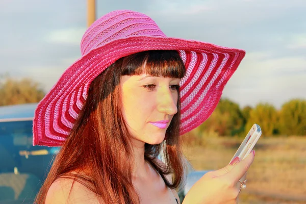 Beautiful girl in the hat reads the message on the phone — Stock Photo, Image