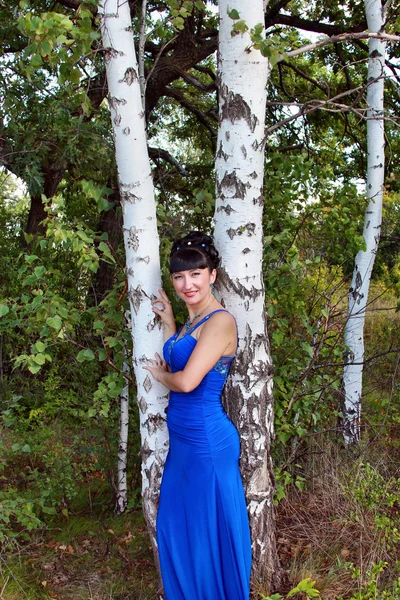 Счастливая девушка в длинном голубом платье стоит у березы — стоковое фото