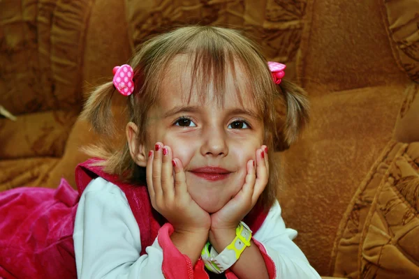Kleines lächelndes Mädchen, die Hände am Kinn, auf dem Sofa liegend — Stockfoto