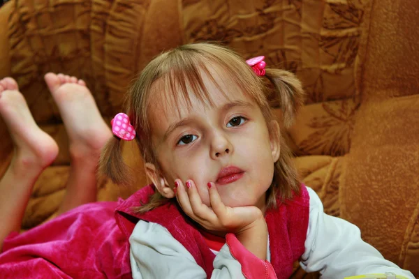 Little serious girl, hand propping chin, lying on the sofa — Stock Photo, Image