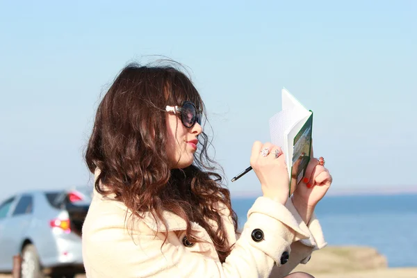 Chica joven escribiendo en un cuaderno, en un fondo de coche —  Fotos de Stock