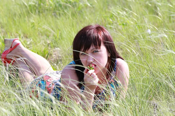 Девушка лежит в траве и ест клубнику — стоковое фото