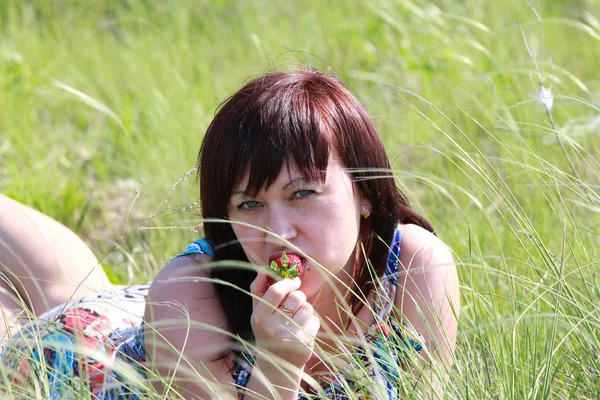 Eine junge brünette Frau isst eine Erdbeere, während sie in der Gr — Stockfoto