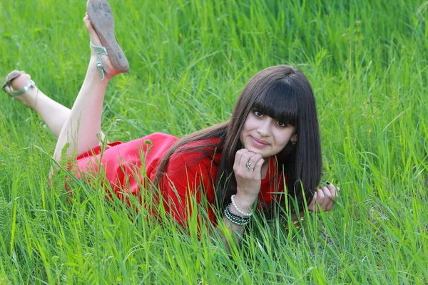 Dziewczyna w czerwonej sukni jest w stanie spoczynku na zielonej trawie — Zdjęcie stockowe