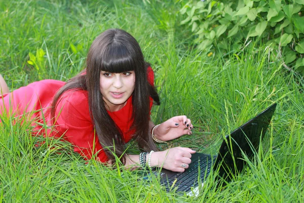 Молодая девушка лежит на траве с ноутбуком — стоковое фото