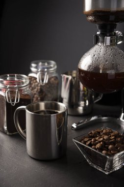 Elektrik süpürgesi, sifon ya da sifon kahve makinesi olarak da bilinir. Metalik fincan ve kavrulmuş kahve çekirdekleri kırsal siyah taş masada.. 