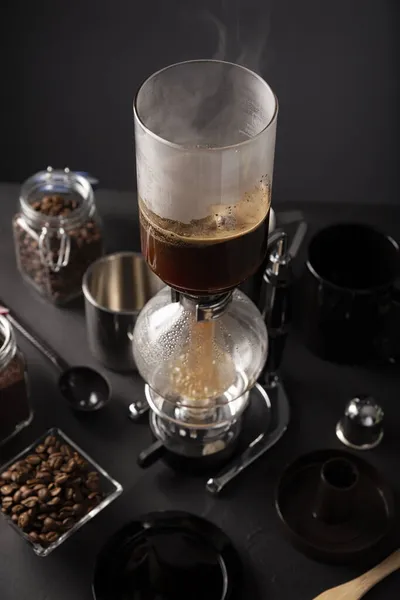 Vacuum coffee maker also known as vac pot, siphon or syphon coffee maker and toasted coffee beans on rustic black stone table.