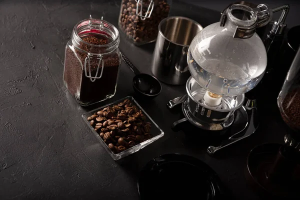 Vacuum coffee maker also known as vac pot, siphon or syphon coffee maker and toasted coffee beans on rustic black stone table. Copy space for your text