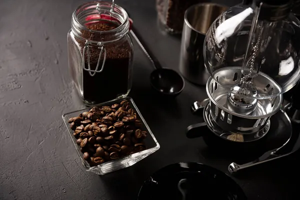 Vacuum coffee maker also known as vac pot, siphon or syphon coffee maker and toasted coffee beans on rustic black stone table. Copy space for your text