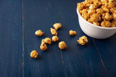 Caramel Popcorn in white bowl on rustic blue wooden table. Close up. Copy space for your text
