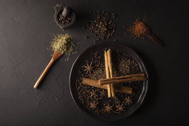 Dokulu siyah arkaplandaki çeşitli baharatların seçimi. Biber, kakule, karanfil, tarçın, yıldız anis, susuz maydanoz.