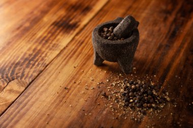 Kırsal ahşap zemin üzerinde küçük bir Molcajete (havan ve tokmağın geleneksel Meksika versiyonu) kara biber taneleri