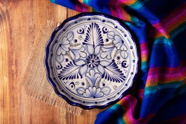 Meksika mutfağı arka planı, renkli geleneksel kumaş ve ahşap kırsal masada boş talavera tarzı tabak. Düz yatıyordu