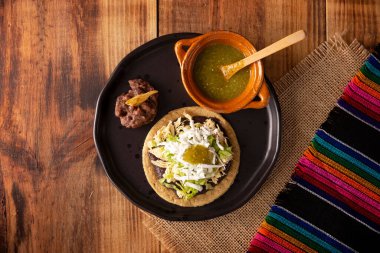 Sopes de Pollo. Traditional homemade Mexican appetizer prepared with fried corn dough covered with refried beans, green or red sauce, lettuce, cheese, onion and shredded chicken