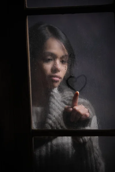 Retrato de mulher desenho coração na janela molhada — Fotografia de Stock