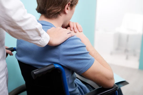 Docteur consolant jeune homme assis en fauteuil roulant — Photo