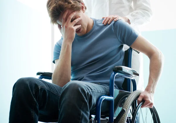 Dottore consolante giovane uomo seduto in sedia a rotelle — Foto Stock