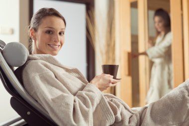 sıcak bir sağlıklı içecek tutan gülümseyerek ve dinlendirici spa adlı genç kadın.