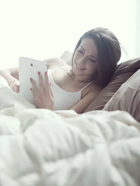 Mujer disfrutando con una tableta digital en la cama por la mañana —  Fotos de Stock