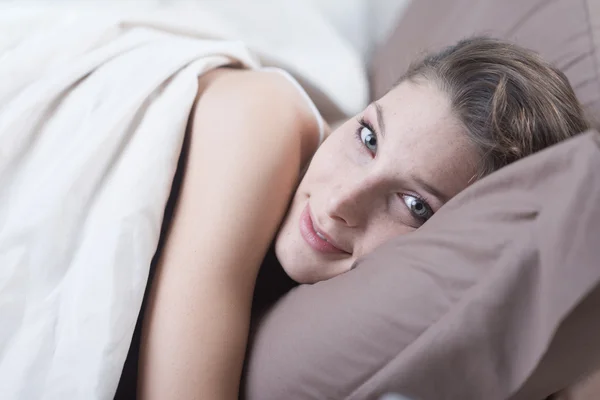 Giovane donna sdraiata a letto e sorridente alla fotocamera — Foto Stock