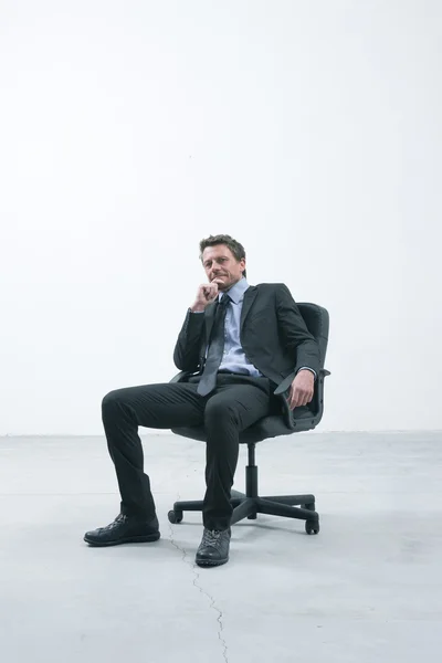 Elegante zakenman zittend op een stoel van het Bureau in een lege ruimte op zoek naar camera. — Stockfoto