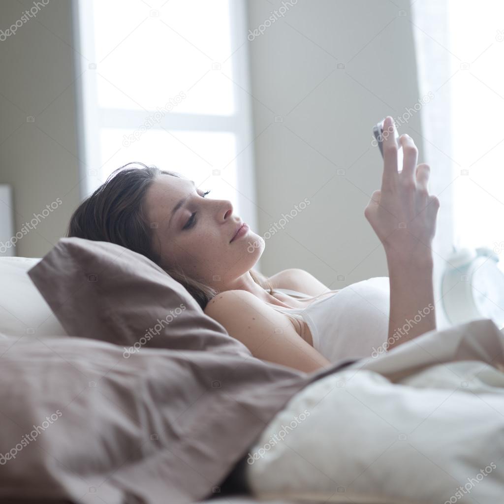Young woman lying on the bed at home and receiving a text