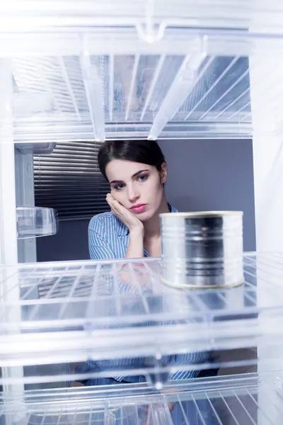 Traurige Frau blickt auf eine Dose in ihrem leeren Kühlschrank — Stockfoto