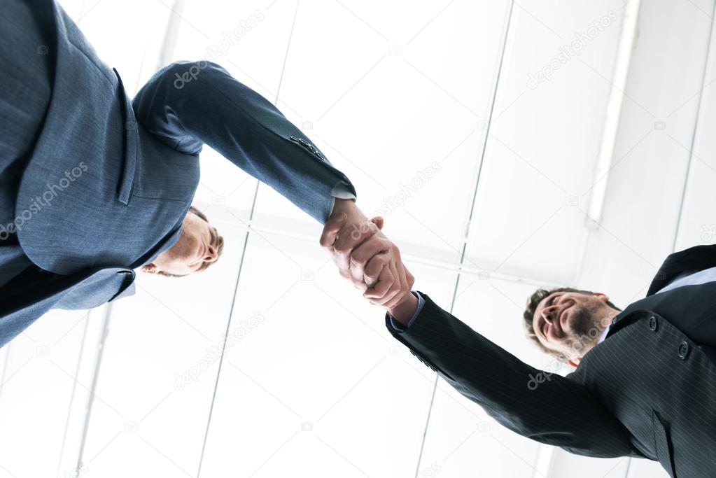 Confident young businessmen smiling and shaking hands bottom view.