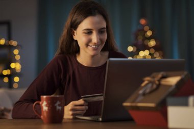 Mutlu genç bir kadın Noel 'de kredi kartıyla online alışveriş yapıyor.
