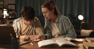 Genç öğretmen bir öğrenciye ev ödevinde yardım ediyor, onu kontrol ediyor ve düzeltiyor, evde eğitim kavramı.