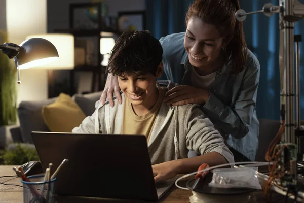 Teenagers learning 3D modeling and using a 3D printer, the boy is using a laptop and the girl is helping him