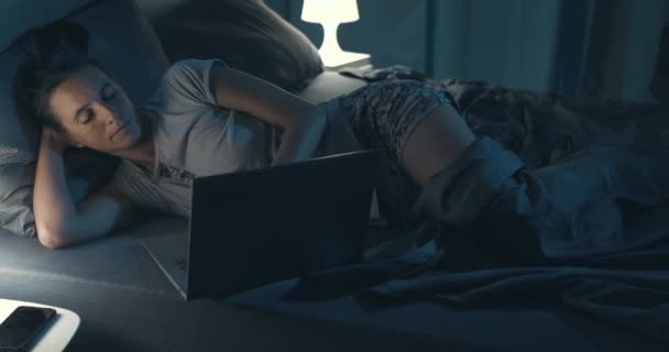 Donna sdraiata a letto e in collegamento con il suo computer portatile — Video Stock