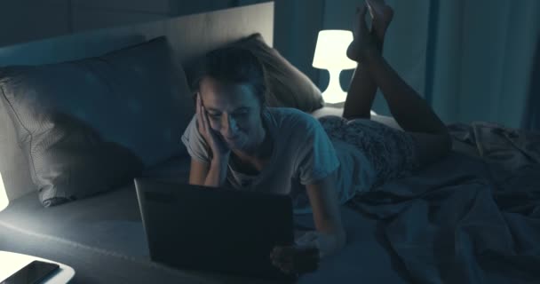 Жінка лежить в ліжку і з'єднується з ноутбуком — стокове відео