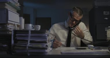 İş adamı gece geç saatlere kadar çalışıyor ve telefonlara cevap veriyor.